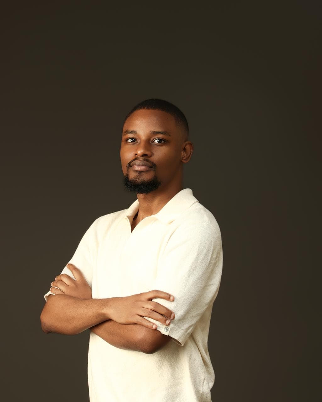 Kehinde Abiuwa standing side-on with his arms folded, in a cream polo