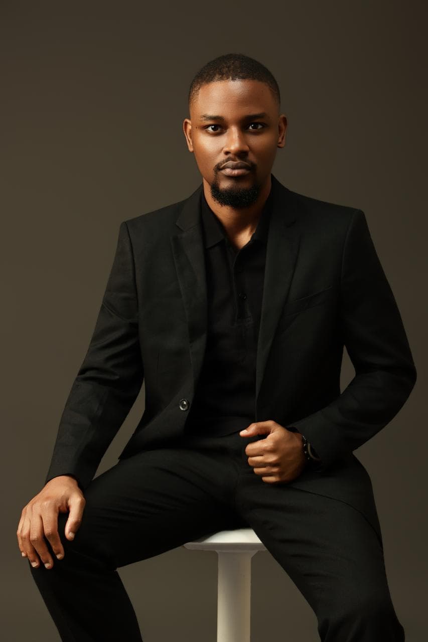 Kehinde Abiuwa seated on a stool in a black suit